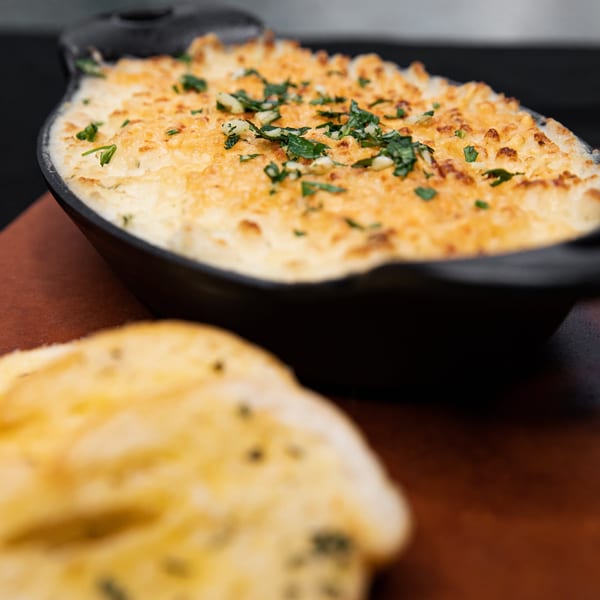 Creamy baked dip with melted cheese and herbs in a black dish, served with toasted bread.