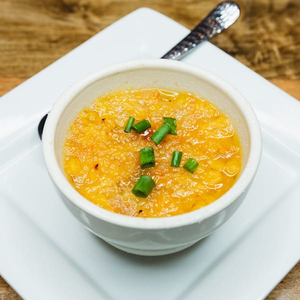 A white bowl of orange-yellow grits, topped with chopped green onions, on a white rectangular plate.