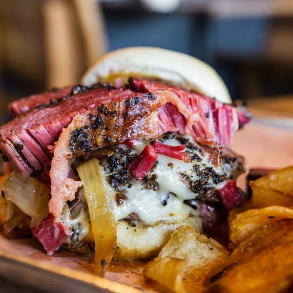 A close-up of a Downing Street Pour House burger with pastrami, melted cheese, and chips.