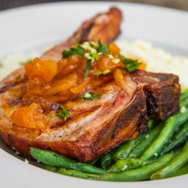 Grilled pork chop with apricot glaze, green beans, and mashed potatoes on a white plate.