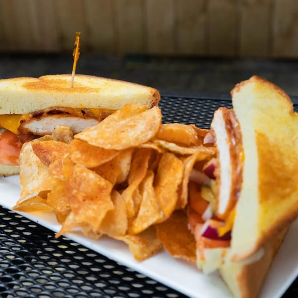 Grilled chicken sandwich with melted cheese, tomato, and onion, served with a side of potato chips.