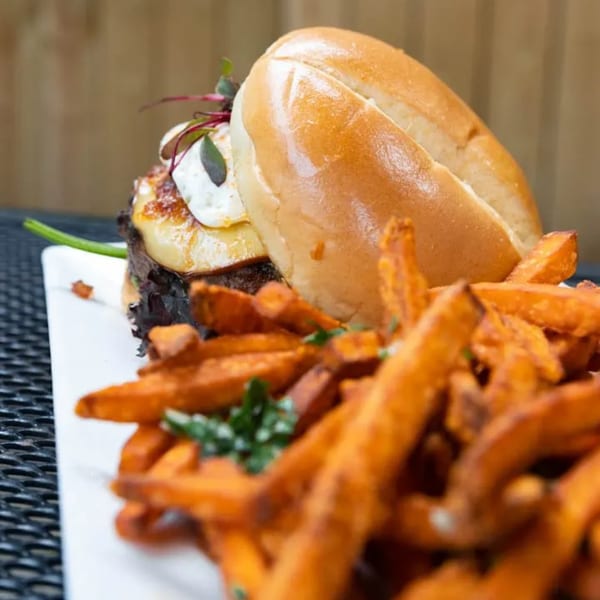 A burger with grilled pineapple and a side of sweet potato fries on a white plate.