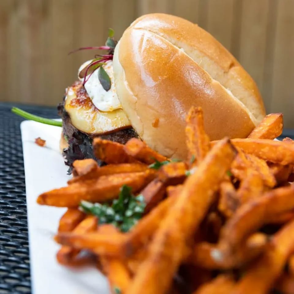 A burger with grilled pineapple and a side of sweet potato fries on a white plate.