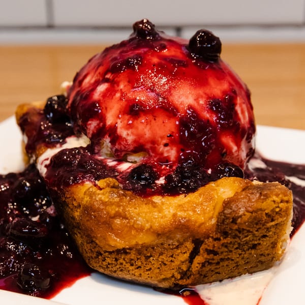 Warm American dessert with a scoop of vanilla ice cream and berry compote on a white plate.