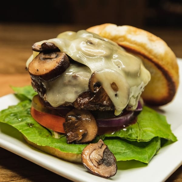 A mushroom and Swiss burger with lettuce, tomato, and red onion on a white plate.